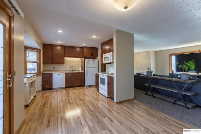 kitchen featuring light wood-style flooring, white appliances, a sink, open floor plan, and light countertops