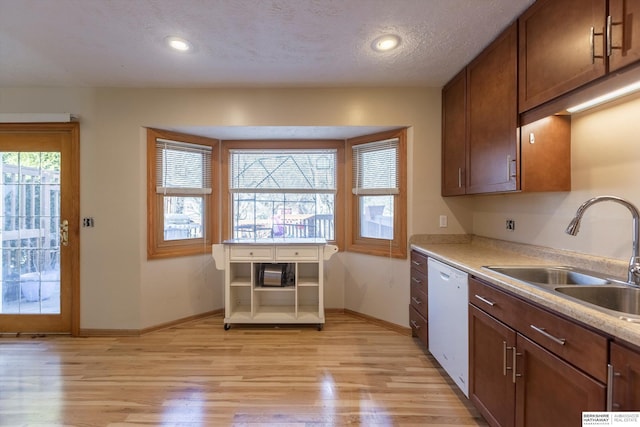 kitchen with baseboards, dishwasher, light countertops, light wood-style floors, and a sink