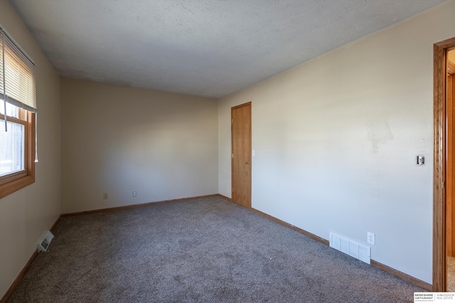 empty room with carpet, visible vents, a textured ceiling, and baseboards