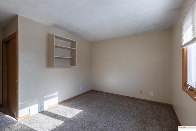 carpeted spare room with a textured ceiling, visible vents, and baseboards