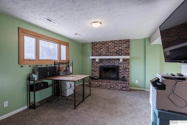 carpeted office featuring a textured ceiling, a brick fireplace, visible vents, and baseboards