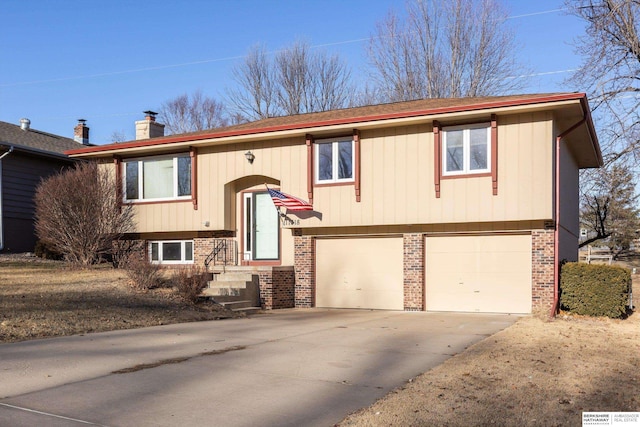 split foyer home featuring driveway, a garage, a chimney, and brick siding