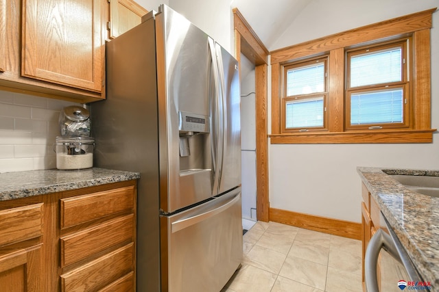 kitchen with brown cabinets, decorative backsplash, appliances with stainless steel finishes, vaulted ceiling, and baseboards