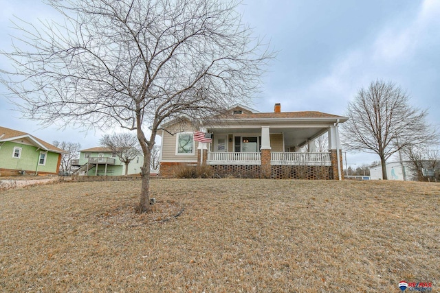 view of front of home featuring covered porch, brick siding, a chimney, and a front yard