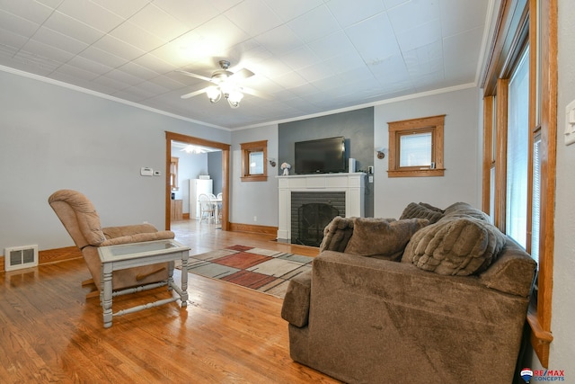 living area featuring light wood finished floors, visible vents, ornamental molding, a brick fireplace, and baseboards