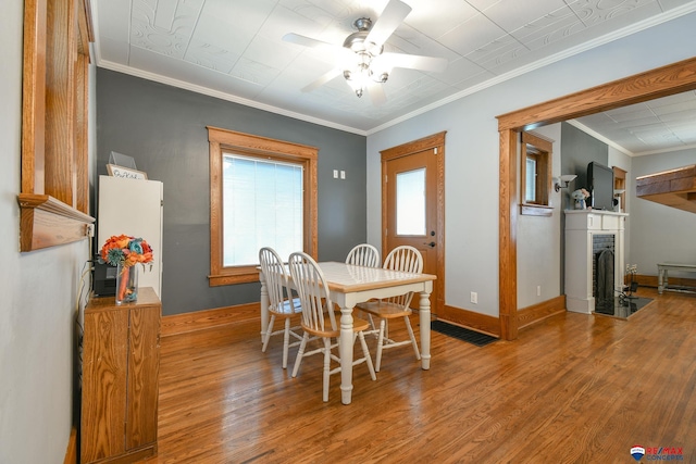 dining area with baseboards, a fireplace with flush hearth, ceiling fan, wood finished floors, and crown molding