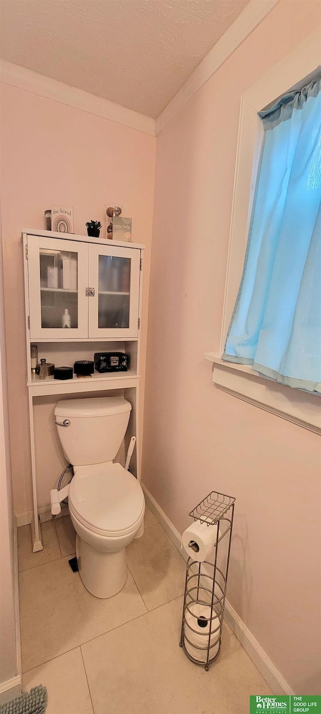 bathroom with tile patterned flooring, baseboards, crown molding, and toilet