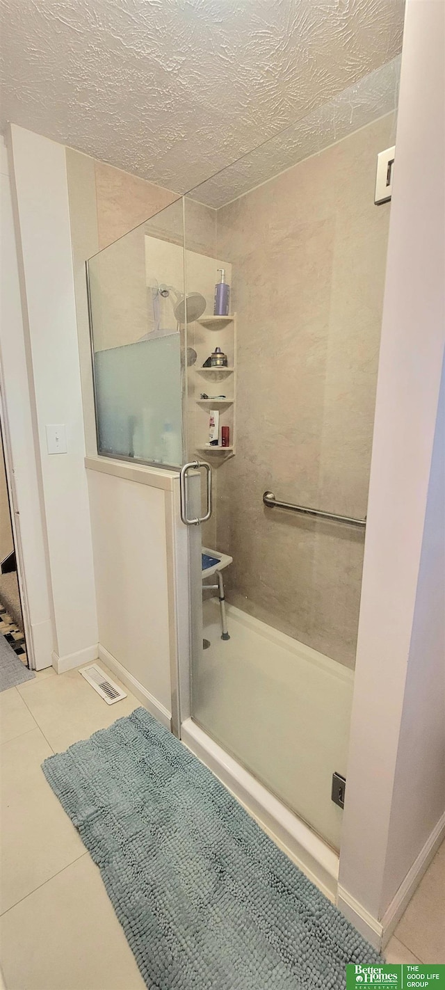 full bathroom featuring a textured ceiling, tile patterned flooring, visible vents, baseboards, and a stall shower