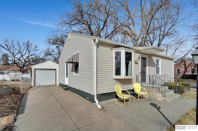 view of front of house with an outdoor structure, concrete driveway, fence, and a detached garage