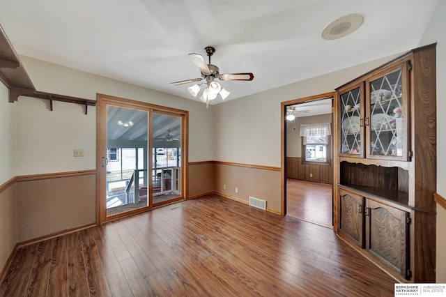 unfurnished dining area with visible vents, wainscoting, a ceiling fan, and wood finished floors