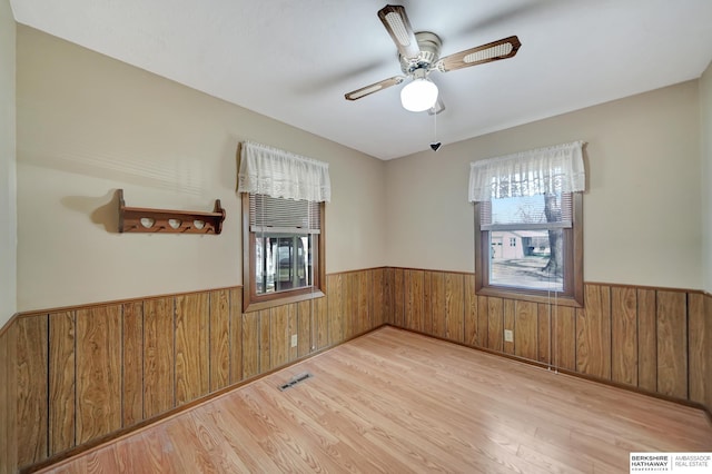 unfurnished room featuring visible vents, wainscoting, wood walls, and wood finished floors