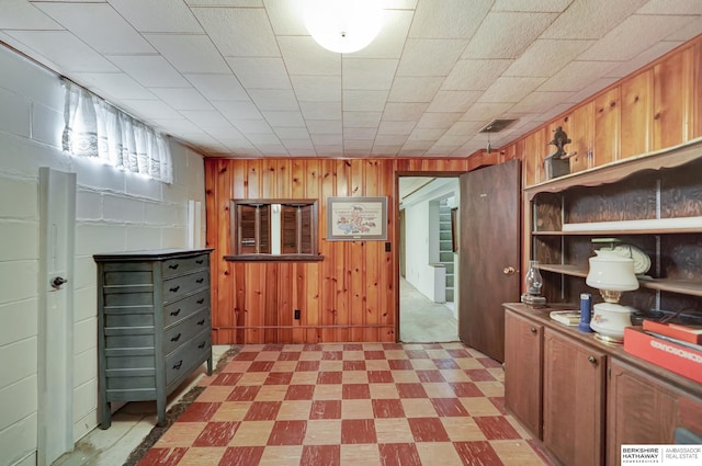 interior space featuring wooden walls, concrete block wall, light floors, open shelves, and brown cabinets