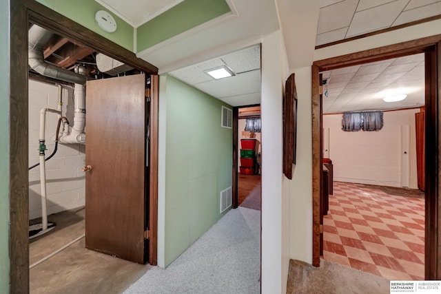 hall with a drop ceiling, visible vents, and concrete block wall