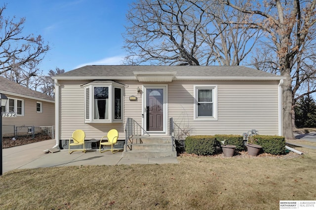 bungalow-style house featuring roof with shingles and a front yard