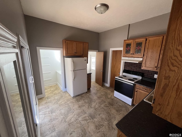 kitchen featuring white appliances, tasteful backsplash, brown cabinetry, dark countertops, and under cabinet range hood