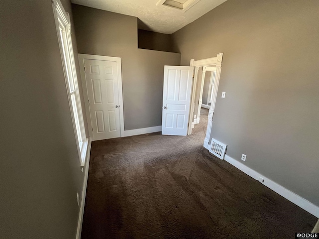 unfurnished bedroom featuring lofted ceiling, visible vents, dark carpet, and baseboards