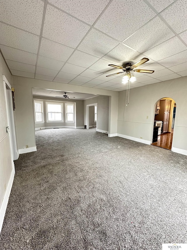 empty room featuring baseboards, arched walkways, ceiling fan, carpet flooring, and a paneled ceiling