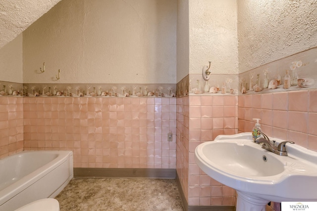 bathroom featuring a bath, a textured wall, a sink, and tile walls