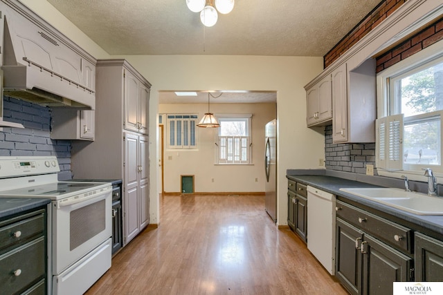 kitchen featuring white appliances, dark countertops, a sink, light wood-style floors, and backsplash