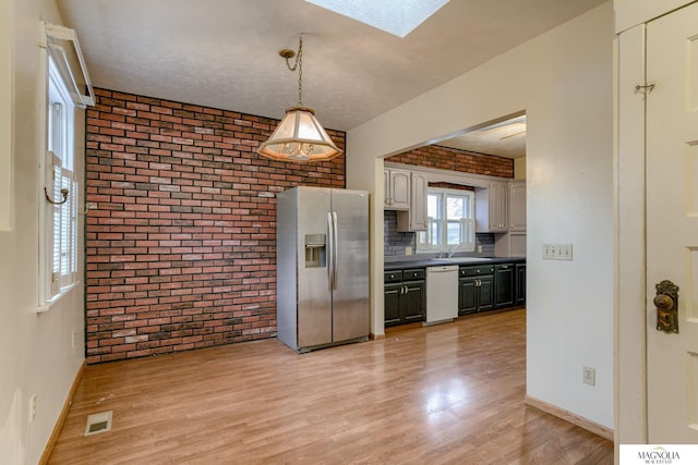 kitchen featuring visible vents, dishwasher, stainless steel refrigerator with ice dispenser, and brick wall