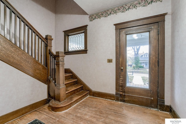 foyer entrance featuring lofted ceiling, stairway, baseboards, and wood finished floors