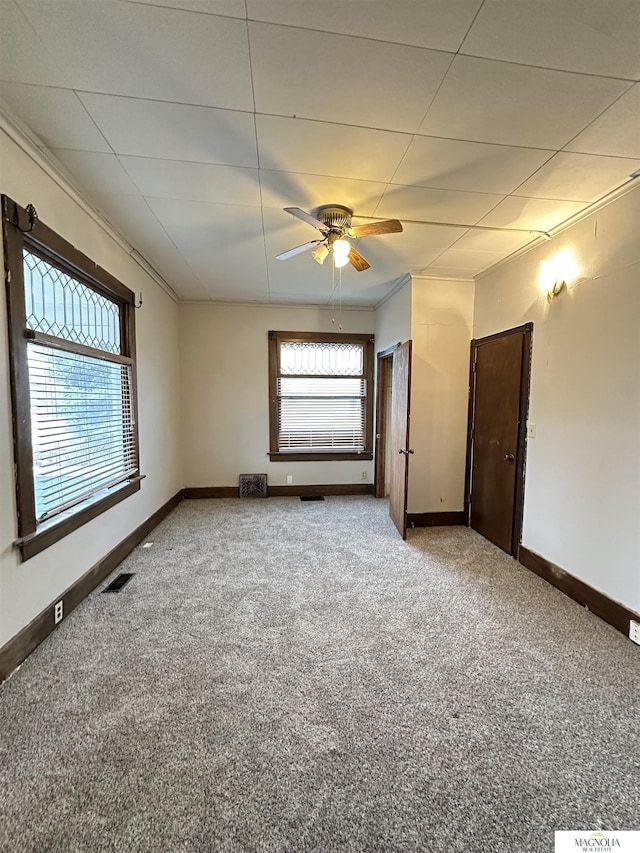 carpeted empty room featuring ornamental molding, visible vents, baseboards, and a ceiling fan