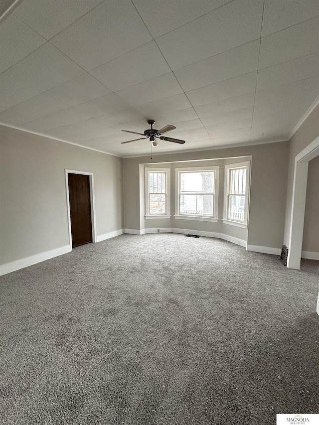 carpeted empty room with a paneled ceiling, ceiling fan, baseboards, and ornamental molding