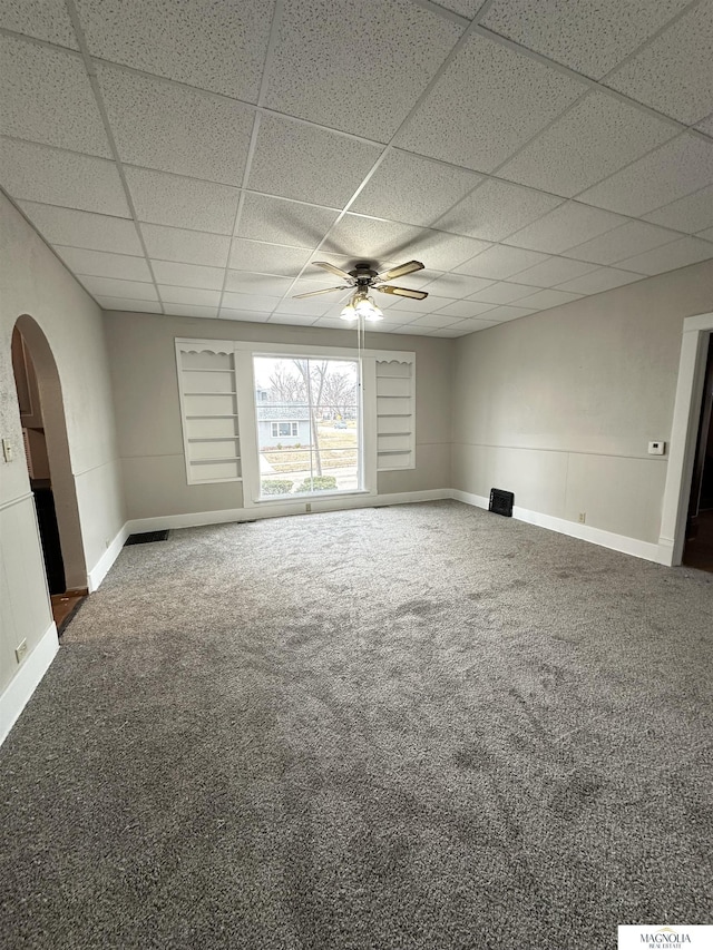 carpeted empty room with arched walkways, ceiling fan, a paneled ceiling, and baseboards