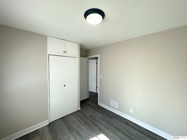 unfurnished bedroom featuring dark wood finished floors, a closet, visible vents, a textured ceiling, and baseboards