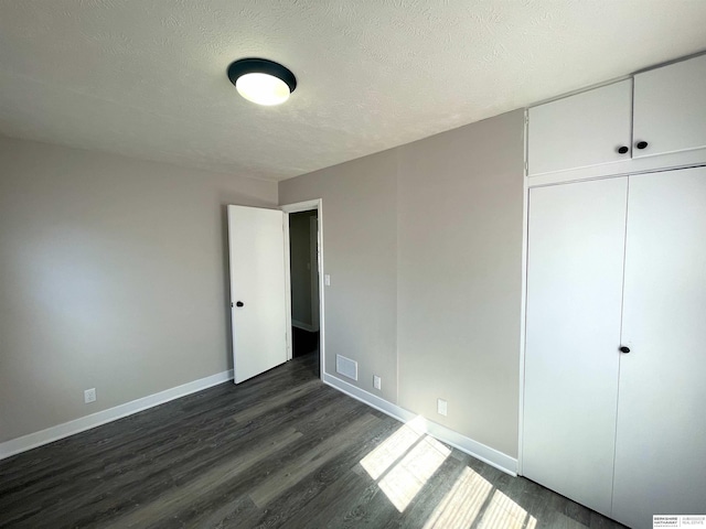 unfurnished bedroom featuring baseboards, visible vents, dark wood finished floors, and a textured ceiling