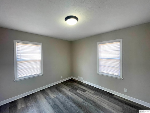 spare room with dark wood-style floors, visible vents, and baseboards