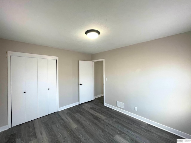 unfurnished bedroom featuring visible vents, a closet, baseboards, and dark wood-type flooring