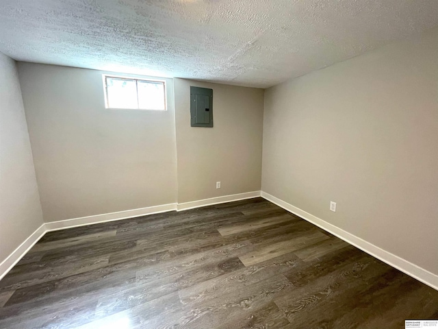 below grade area with a textured ceiling, electric panel, baseboards, and dark wood-type flooring