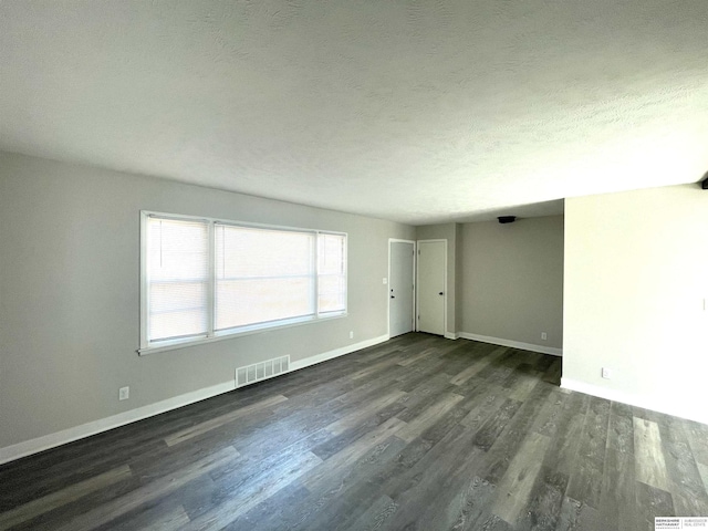 unfurnished room featuring dark wood-style floors, visible vents, a textured ceiling, and baseboards