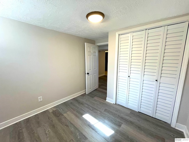 unfurnished bedroom with a textured ceiling, dark wood-type flooring, a closet, and baseboards