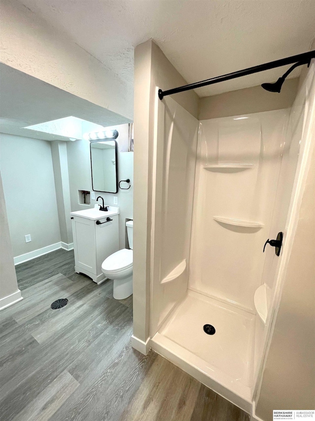 bathroom with toilet, vanity, a shower stall, wood finished floors, and baseboards