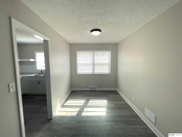 unfurnished room with dark wood-type flooring, visible vents, a sink, and baseboards