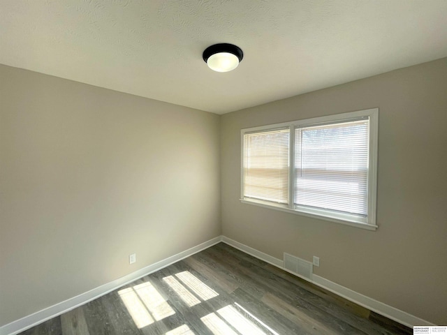 empty room with dark wood-style flooring, visible vents, and baseboards