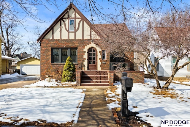 tudor home featuring an outbuilding, covered porch, stucco siding, a garage, and brick siding