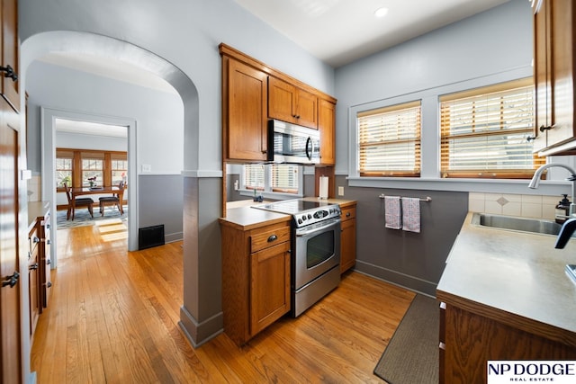 kitchen featuring light wood finished floors, brown cabinets, arched walkways, stainless steel appliances, and a sink