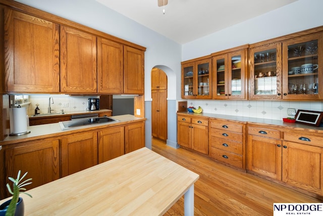 kitchen with brown cabinets, light wood-style flooring, a sink, glass insert cabinets, and black electric cooktop