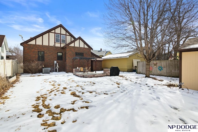 snow covered back of property with brick siding, central AC unit, and fence