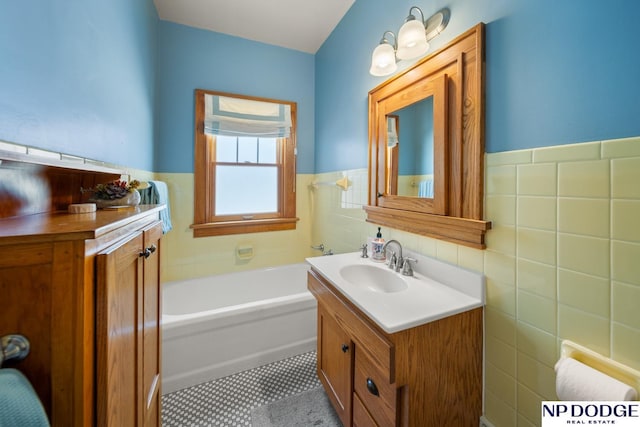 full bath featuring tile patterned floors, tile walls, a wainscoted wall, a bath, and vanity