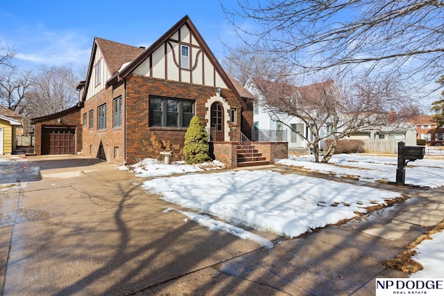 tudor-style house featuring brick siding, a shingled roof, stucco siding, driveway, and an attached garage