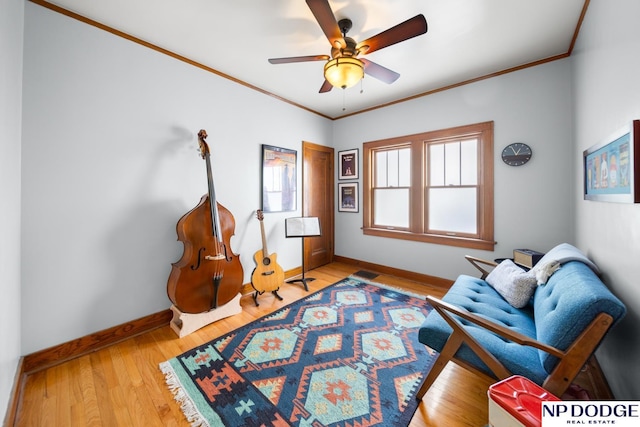 living area featuring a ceiling fan, crown molding, baseboards, and light wood-type flooring