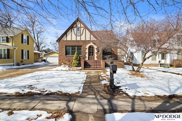 tudor house with stucco siding, a detached garage, a porch, an outdoor structure, and brick siding