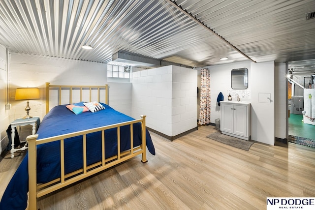 bedroom with visible vents, concrete block wall, light wood-type flooring, and a sink