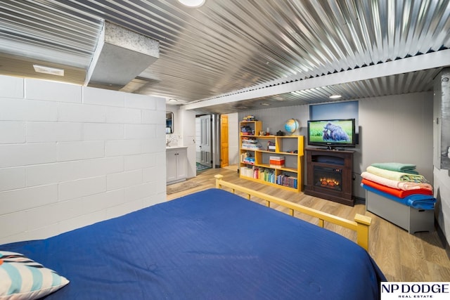 bedroom with concrete block wall, a lit fireplace, and wood finished floors