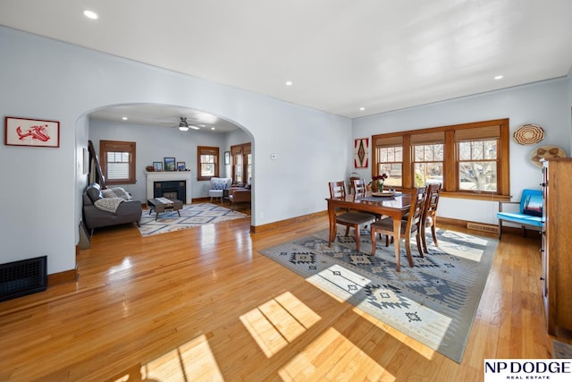 dining room with visible vents, hardwood / wood-style floors, recessed lighting, arched walkways, and a glass covered fireplace