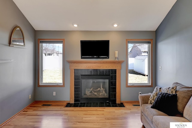 living area featuring visible vents, baseboards, wood finished floors, and a tiled fireplace